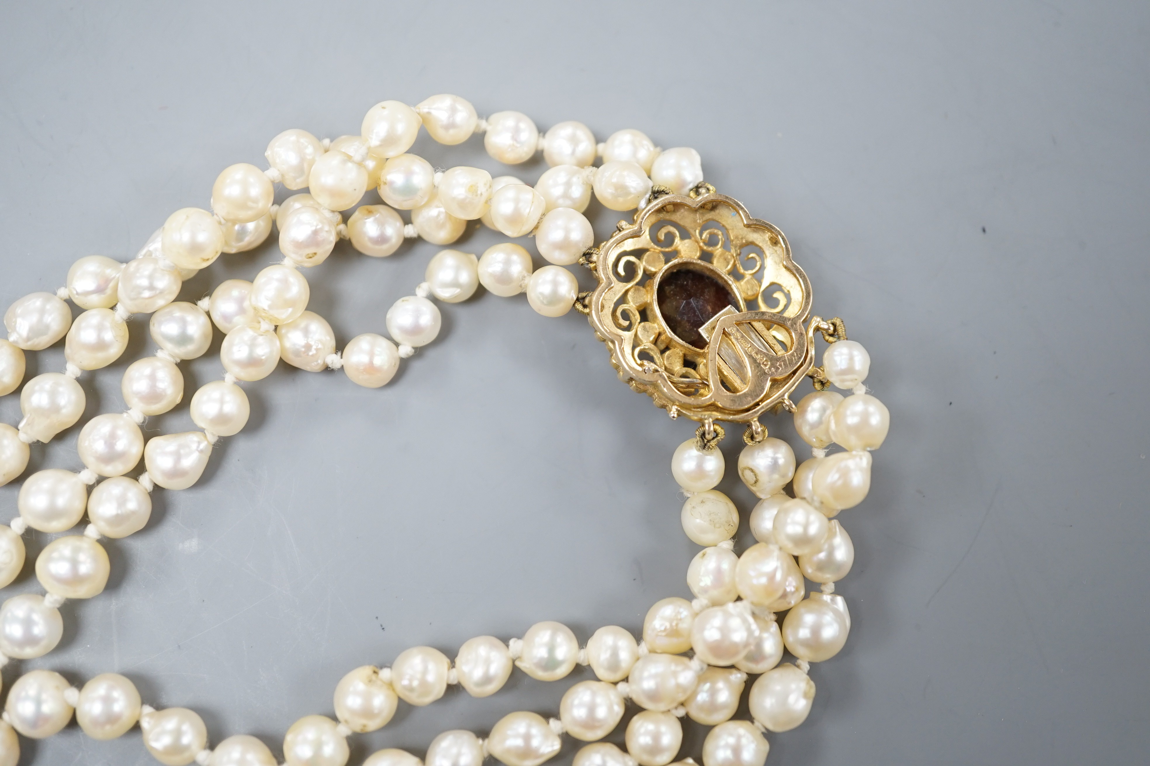 A 1960's triple strand cultured pearl necklace, with garnet and seed pearl set 9ct gold clasp, 48cm.
